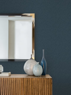 A wooden sideboard with four decorative vases in different shapes and colors sits below a large rectangular mirror on a wall covered in Hilbert Geometric Wallpaper by York Wallcoverings.