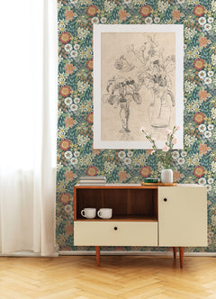 A sideboard with two mugs sits against a wall adorned in Karina Wildflower Garden Wallpaper by York Wallcoverings. Above is a framed black-and-white flower sketch, while a vase with pink flowers rests on the sideboard; white curtains hang to the left.