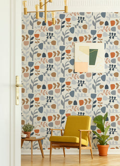 A mid-century modern room featuring a yellow armchair, a small wooden table with two potted plants, and a green potted plant on the floor, with the wall adorned in York Wallcoverings’ Juni Abstract Tulips Wallpaper and geometric art.