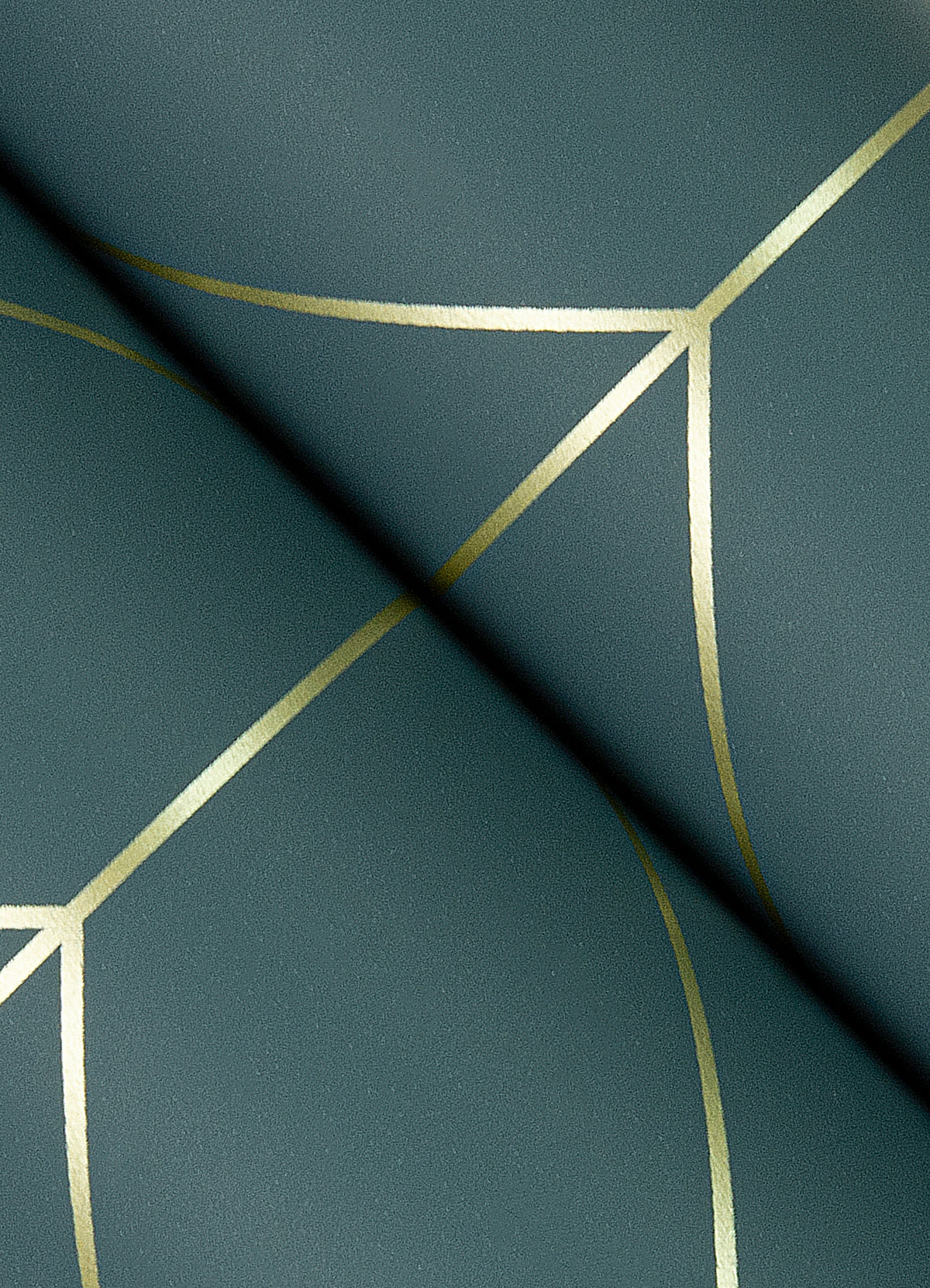 A close-up view of York Wallcoverings’ Sander Geometric Wallpaper shows a green surface adorned with intersecting gold geometric lines that form a modern, abstract pattern, while a dark shadow crosses the design diagonally.