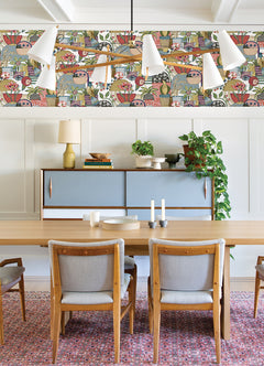Dining room with a wooden table, gray chairs, sideboard, leafy plant, candlesticks, and Fika Blissful Birds & Blooms Wallpaper by York Wallcoverings. A modern chandelier hangs above the table over a red-patterned rug.