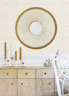 A feature wall adorned with Scout Floral Ogee Wallpaper by York Wallcoverings forms a stylish backdrop above a light wood cabinet. On the cabinet are modern gold and glass candlesticks, a small vase with greenery, and a white chair.