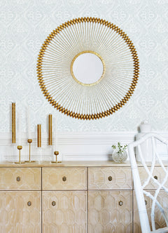 The wall behind a light wood cabinet is adorned with Scout Floral Ogee Wallpaper by York Wallcoverings, while glass candle holders and a small vase sit on top of the cabinet. A white chair is partially visible in the foreground.