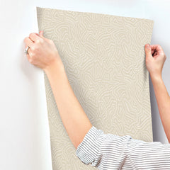 A person with a striped sleeve uses both hands to apply Hollenback Dotted Abstract Wallpaper by York Wallcoverings to a white wall.