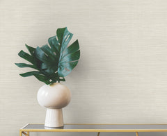 A large monstera leaf in a white vase sits on a gold console table against a neutral-colored Winn Faux Grasscloth Wallpaper by York Wallcoverings with a woven texture.