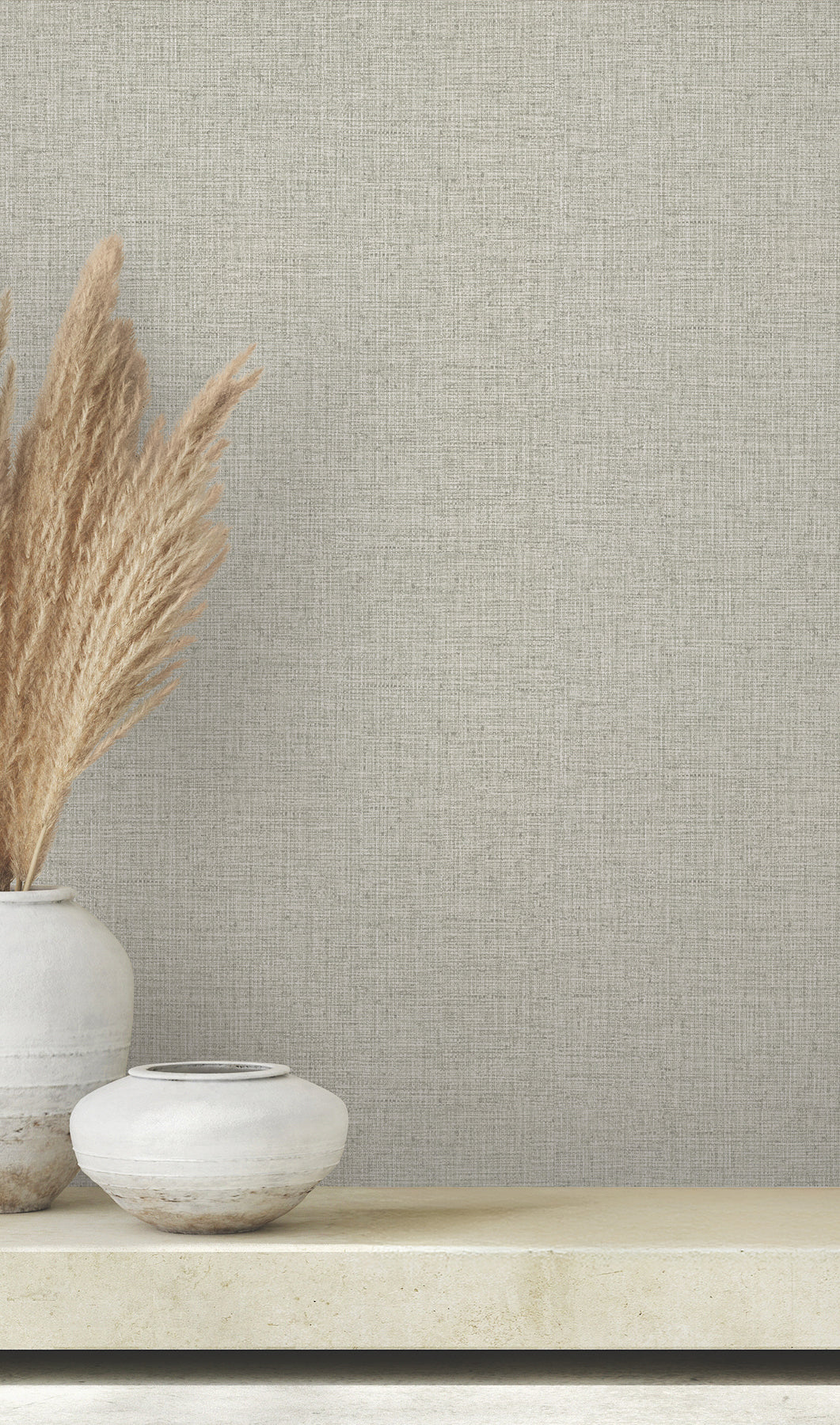 Two decorative vases with pampas grass sit on a shelf against a wall covered in light gray Clarkson Woven Wallpaper by York Wallcoverings.