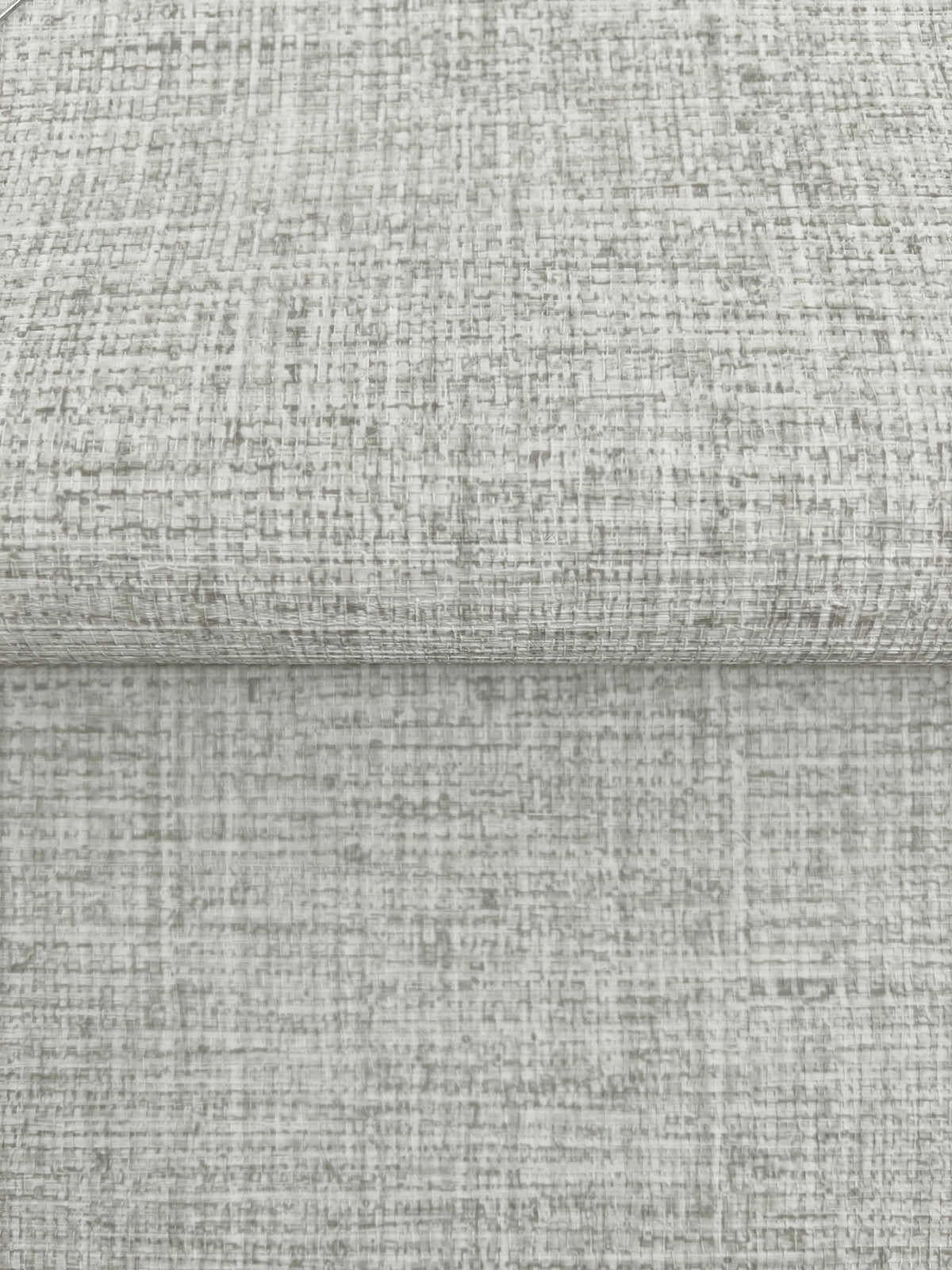 A folded piece of Clarkson Woven Wallpaper featuring a light gray, textured, cross-hatched pattern.
