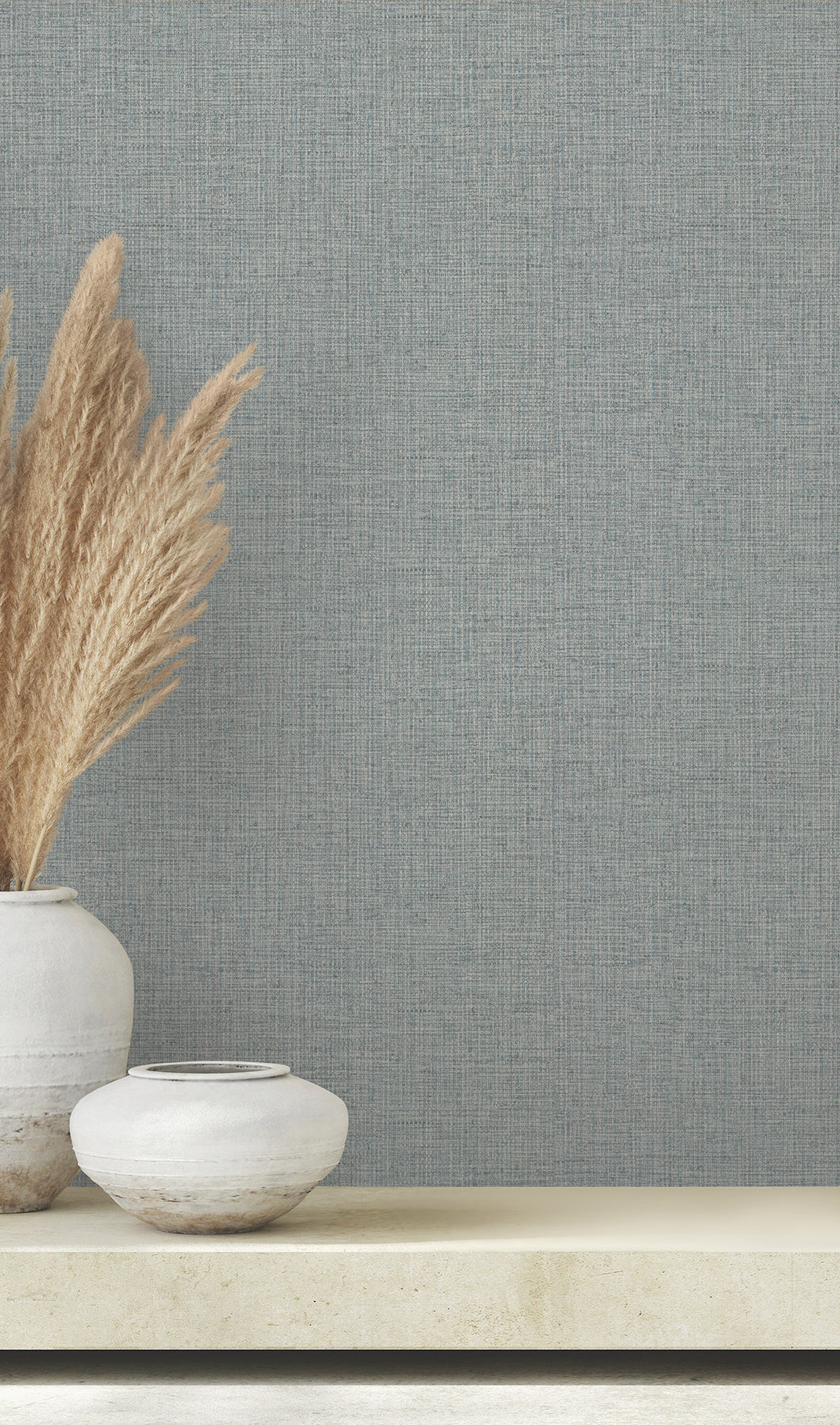 Two white ceramic vases holding dried pampas grass sit on a shelf against Clarkson Woven Wallpaper by York Wallcoverings.