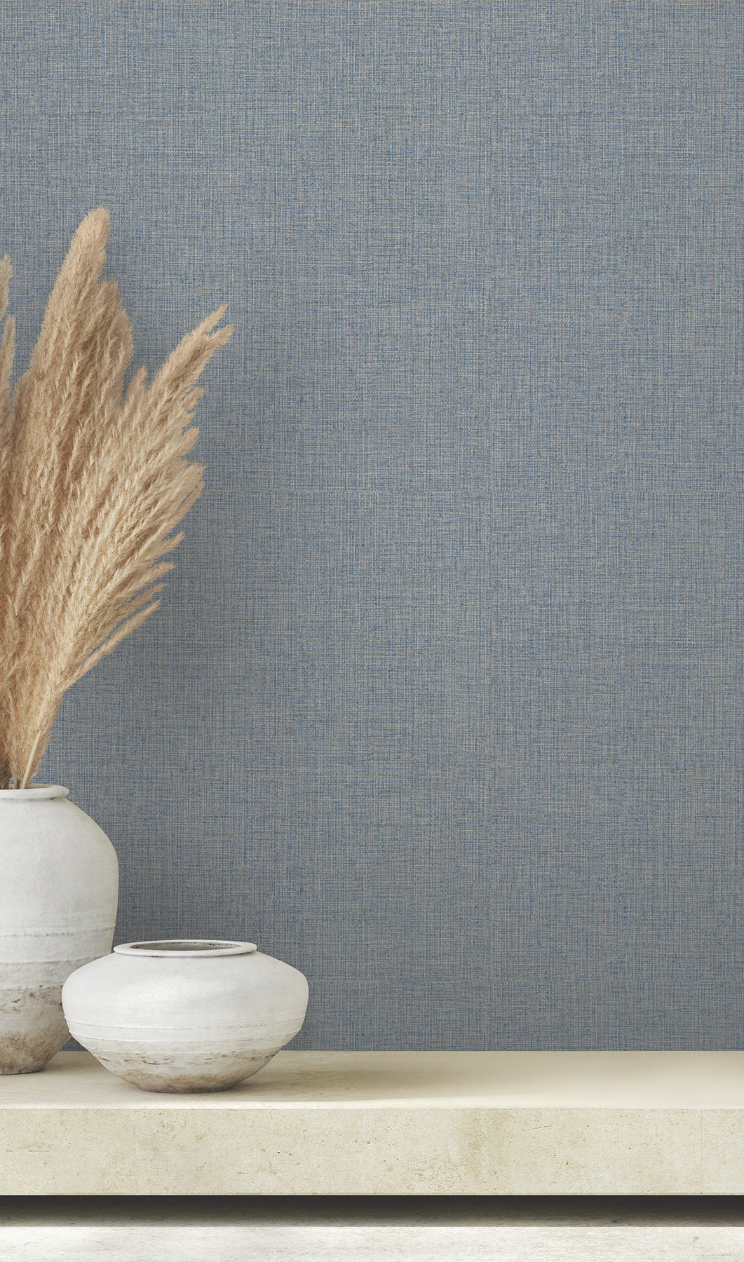 Clarkson Woven Wallpaper in blue with a subtle texture behind two decorative vases holding dried grass.