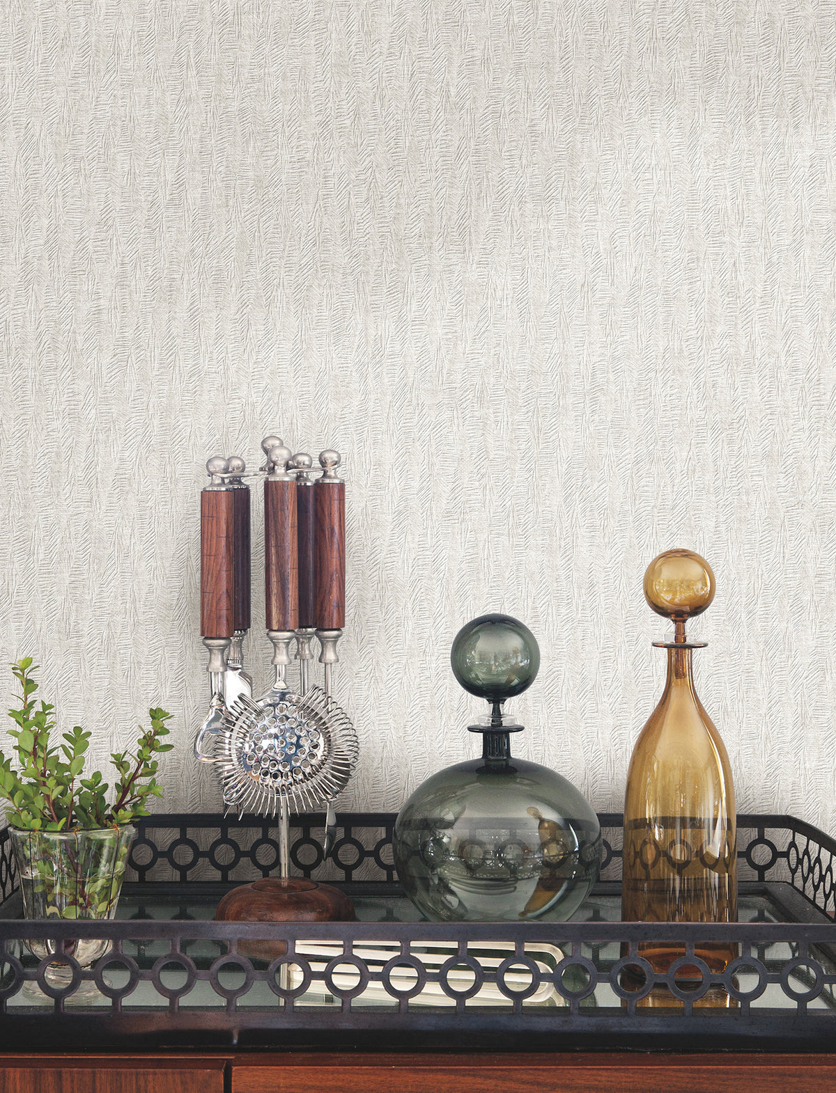 Bryson Feathered Texture Wallpaper in light gray with a fine, feathered texture displayed behind a bar cart holding a glass plant vase, metal bar tools, and two glass decanters.