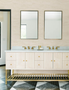 Modern bathroom featuring double sinks, gold fixtures, two rectangular mirrors, a light wood vanity with open slats underneath and a marble countertop, black-and-white checkered floor tiles, and Chesapeake Morgana Stone Wallpaper by York Wallcoverings.