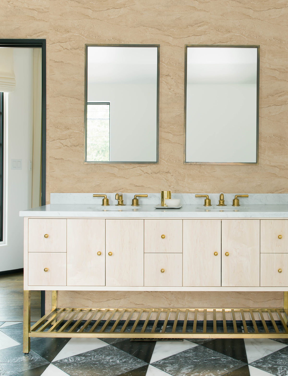 Modern bathroom with a double sink vanity, two mirrors, gold fixtures, and a checkerboard tile floor. The light wood vanity with gold accents is set against beige Chesapeake Morgana Stone Wallpaper by York Wallcoverings.