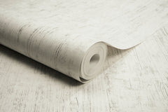 A roll of Chesapeake Ramona Distressed Texture Wallpaper by York Wallcoverings, featuring a light-colored, subtly textured pattern, is partially unrolled on a matching surface.