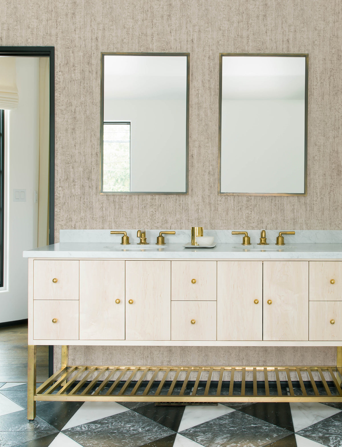 Modern bathroom featuring a double sink vanity with gold faucets and hardware, two rectangular mirrors, light wood cabinets, a black-and-white geometric tile floor, and Chesapeake Ramona Distressed Texture Wallpaper by York Wallcoverings.