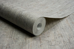 A roll of Chesapeake Ramona Distressed Texture Wallpaper by York Wallcoverings is partially unrolled on a surface featuring a matching wood-like pattern.