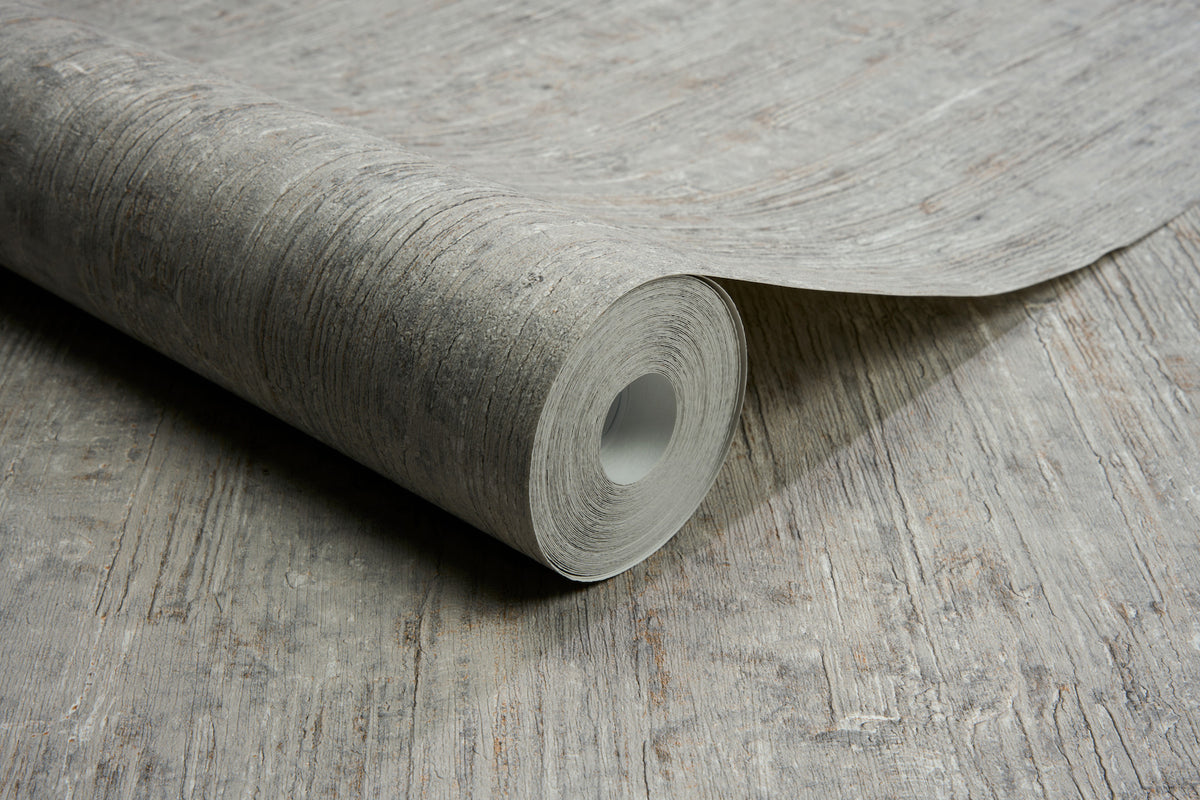 A roll of Chesapeake Ramona Distressed Texture Wallpaper by York Wallcoverings, featuring a textured, wood-like pattern, is partially unrolled on a matching surface.