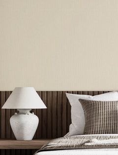 A white table lamp sits on a wooden headboard next to a bed with white and brown striped pillows, with Chesapeake Elijah Texture Wallpaper by York Wallcoverings covering the wall in the background.