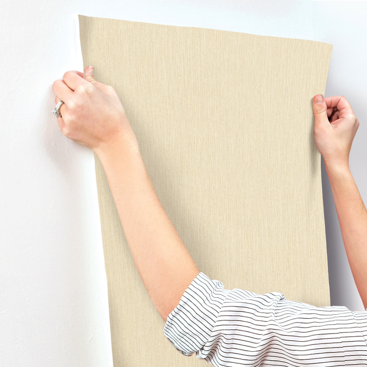 A person with rolled-up sleeves aligns Chesapeake Elijah Texture Wallpaper by York Wallcoverings against a white wall.
