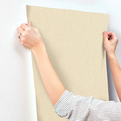 A person with rolled-up sleeves aligns Chesapeake Elijah Texture Wallpaper by York Wallcoverings against a white wall.