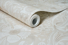 A roll of Chesapeake Liora Floral Trail Wallpaper by York Wallcoverings in light beige, featuring a large, intricate floral pattern, is partially unrolled to display its decorative design on a flat surface.