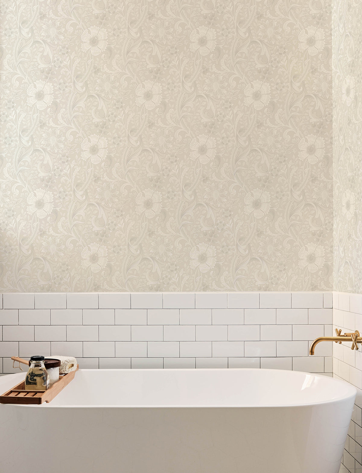A white bathtub with a gold faucet, white subway tile, Chesapeake Liora Floral Trail Wallpaper by York Wallcoverings, and a wooden tray holding soap and a jar are visible in a bright, modern bathroom.