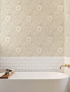 A white bathtub with a wooden tray holding soap and a candle is set against a wall adorned with Chesapeake Liora Floral Trail Wallpaper by York Wallcoverings and white subway tile. A gold faucet is mounted on the wall to the right.