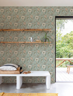 A cozy room featuring York Wallcoverings’ Chesapeake Liora Floral Trail Wallpaper, wooden shelves adorned with plants and decor, a cushioned bench, and a door open to a green outdoor patio with a table and benches.