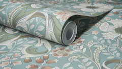 A close-up of the Chesapeake Liora Floral Trail Wallpaper by York Wallcoverings, showing the roll partially unrolled on a matching surface and highlighting its blue, green, white, and beige floral and leaf pattern.