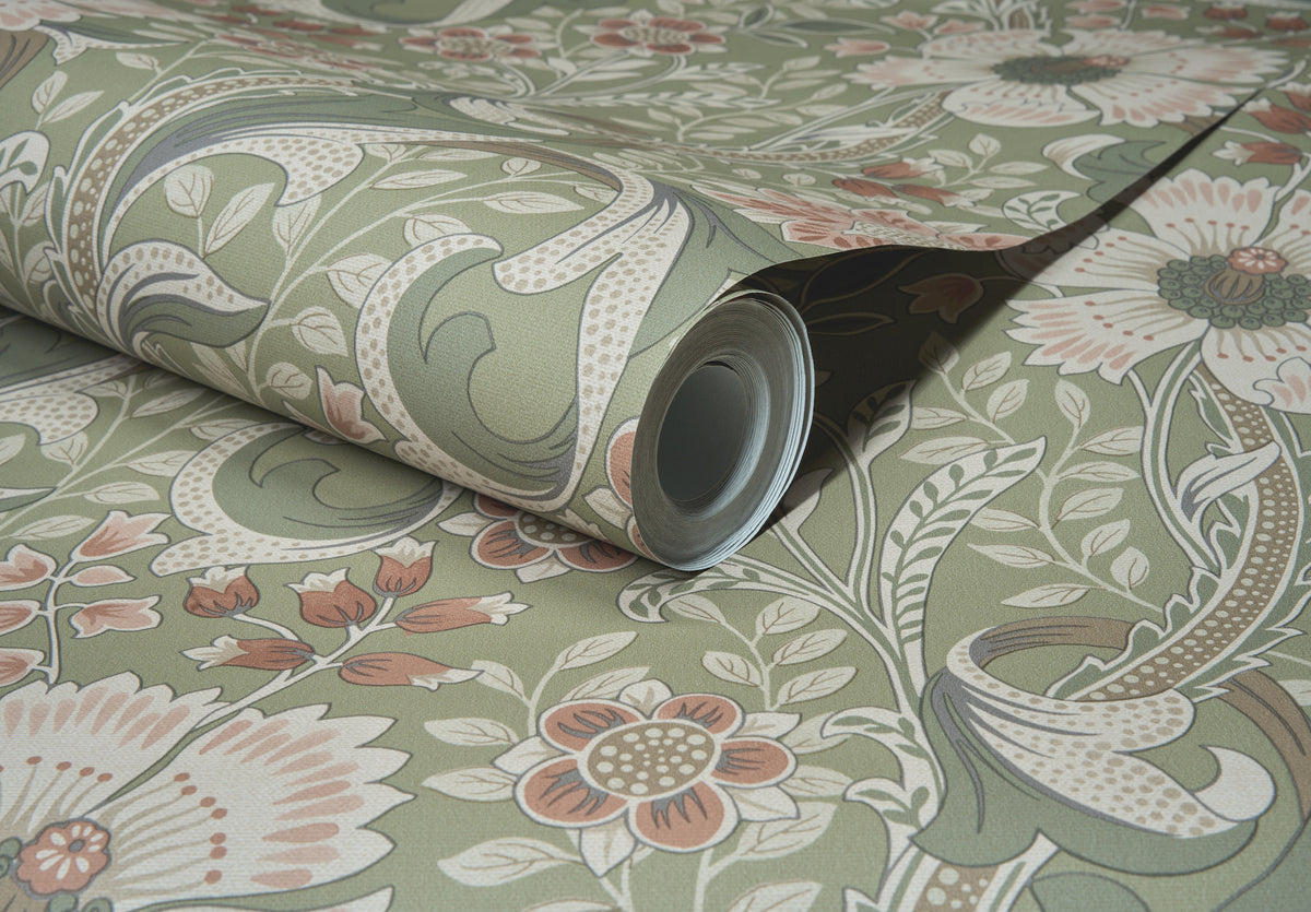 A close-up of a rolled-up Chesapeake Liora Floral Trail Wallpaper by York Wallcoverings, showcasing its green, pink, and beige floral pattern, displayed on a flat surface alongside matching floral wallpaper.