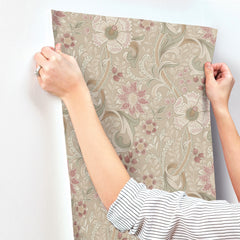 Someone wearing a striped shirt is carefully smoothing Chesapeake Liora Floral Trail Wallpaper by York Wallcoverings onto a white wall with their hands.