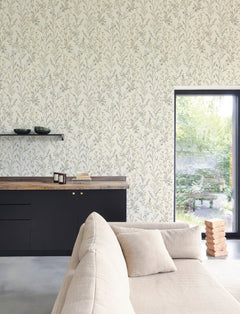 A cozy living room features a beige sofa, black cabinets, and a wooden countertop. Wall shelves hold bowls above the Chesapeake Laverne Wildflowers Wallpaper by York Wallcoverings, while a large window overlooks a green garden. A Jenga game sits on the floor near the window.