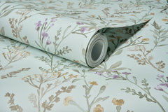 A partially unrolled roll of Chesapeake Laverne Wildflowers Wallpaper by York Wallcoverings, featuring a light blue background adorned with delicate floral patterns in shades of green, purple, and yellow, rests on a flat surface.