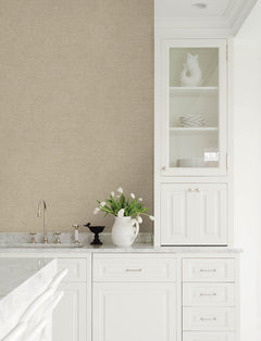 A bright, white kitchen with marble countertops, Chesapeake Harrison Swirling Geometric Wallpaper by York Wallcoverings in light beige on the walls, tulips arranged in a pitcher, and a glass cabinet displaying white dishes alongside a decorative vase.