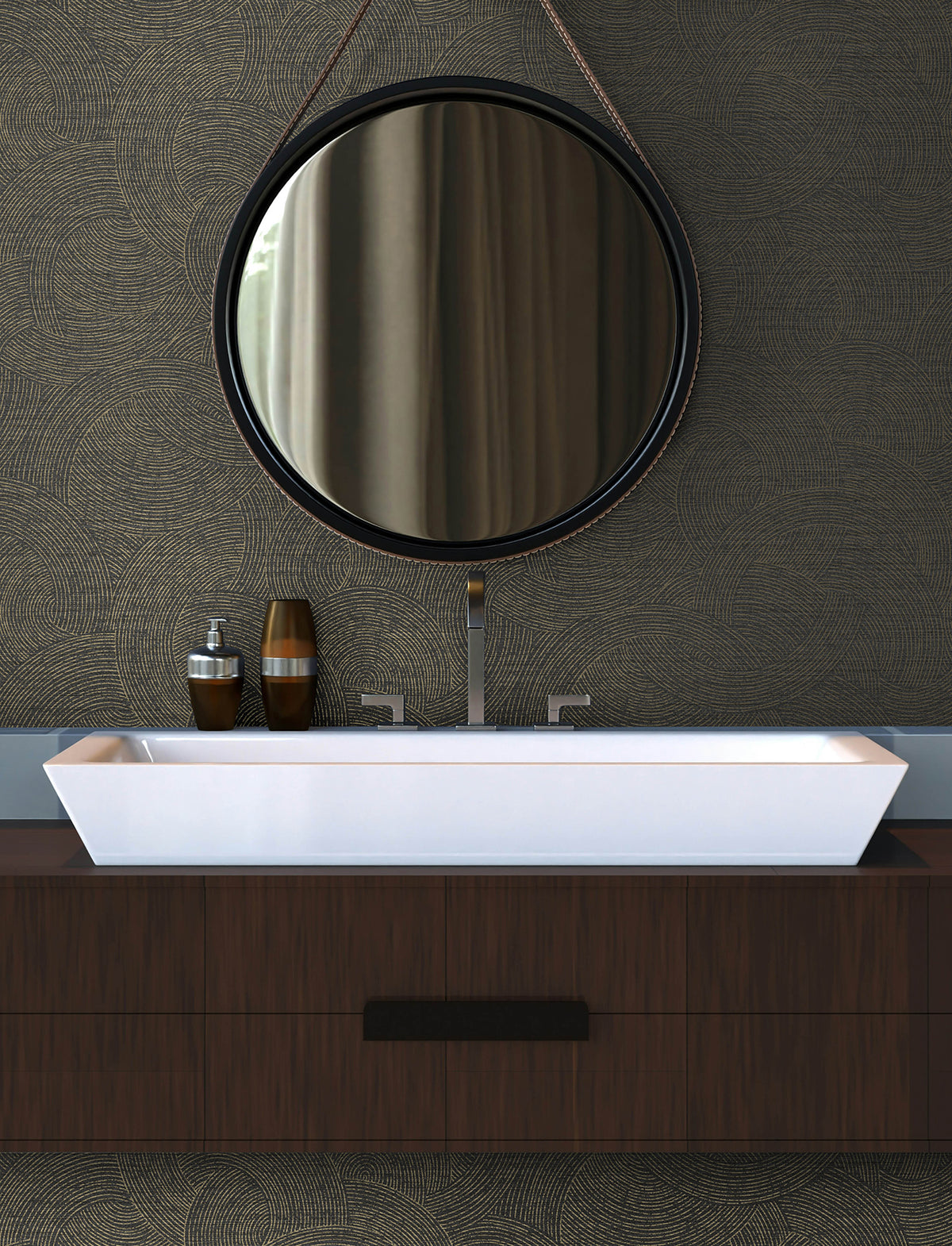 Modern bathroom vanity with a rectangular white sink, two bottles, and a round mirror with a leather strap hanging above, set against Chesapeake Harrison Swirling Geometric Wallpaper by York Wallcoverings.
