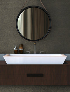 Modern bathroom vanity with a rectangular white sink, two bottles, and a round mirror with a leather strap hanging above, set against Chesapeake Harrison Swirling Geometric Wallpaper by York Wallcoverings.