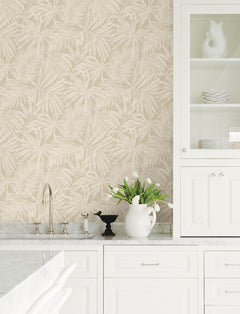 Bright white kitchen with a marble countertop, Chesapeake Sonny Fronds Wallpaper by York Wallcoverings, a sink, and open cabinets with dishes. A white pitcher filled with tulips and a black decorative cup sit on the counter.