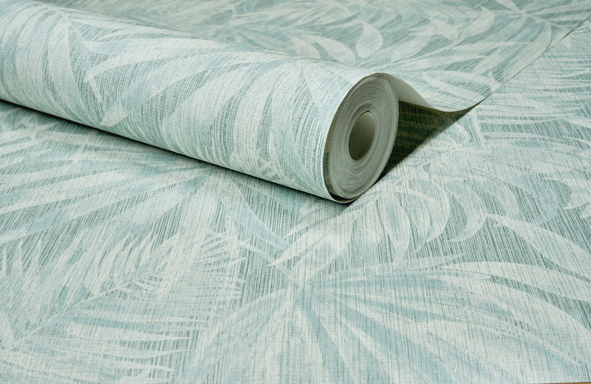 A roll of Chesapeake Sonny Fronds Wallpaper by York Wallcoverings, featuring a light blue and white color palette with a subtle, textured botanical leaf pattern, is partially unrolled on a flat surface to reveal its elegant design.