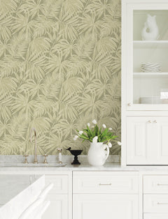 A white kitchen features a marble countertop, Chesapeake Sonny Fronds Wallpaper by York Wallcoverings, white cabinets, a pitcher of white tulips, and a silver faucet. Open shelves display white dishes and decorative items.
