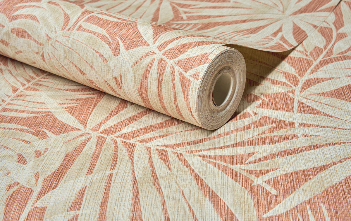 A roll of Chesapeake Sonny Fronds Wallpaper by York Wallcoverings, featuring a beige and terracotta palm leaf pattern, is partially unrolled on a flat surface.