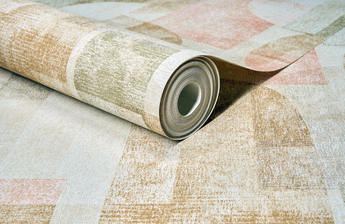 A close-up of a rolled Chesapeake Cassandra Block Geometric Wallpaper by York Wallcoverings, featuring a textured geometric pattern in muted beige, green, and pink tones, partially unrolled on a coordinating surface.