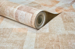 A close-up of a roll of York Wallcoverings Chesapeake Cassandra Block Geometric Wallpaper, featuring a textured geometric pattern in shades of beige and brown, lying on a matching surface.