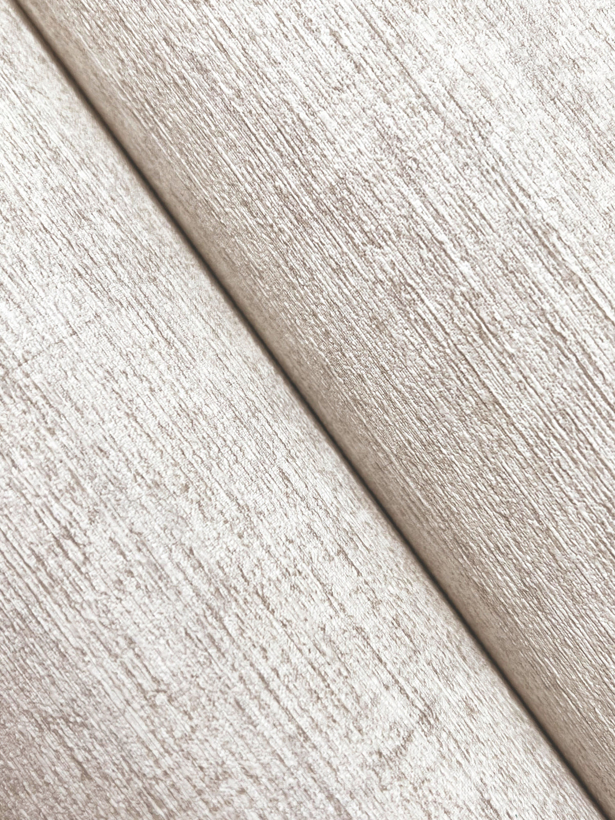 Close-up of two rolls of York Wallcoverings Chesapeake Tansy Distressed Wallpaper placed diagonally, displaying a subtle woodgrain-like pattern and soft sheen in textured beige.