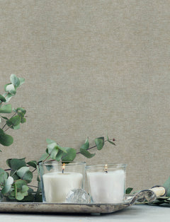 Two white candles in glass holders sit on a silver tray with eucalyptus branches and a faceted crystal, set against a backdrop of Chesapeake Tansy Distressed Wallpaper by York Wallcoverings.