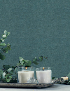 Two white candles in glass holders are lit on a silver tray, surrounded by eucalyptus branches, with York Wallcoverings Chesapeake Tansy Distressed Wallpaper as the blue textured background.