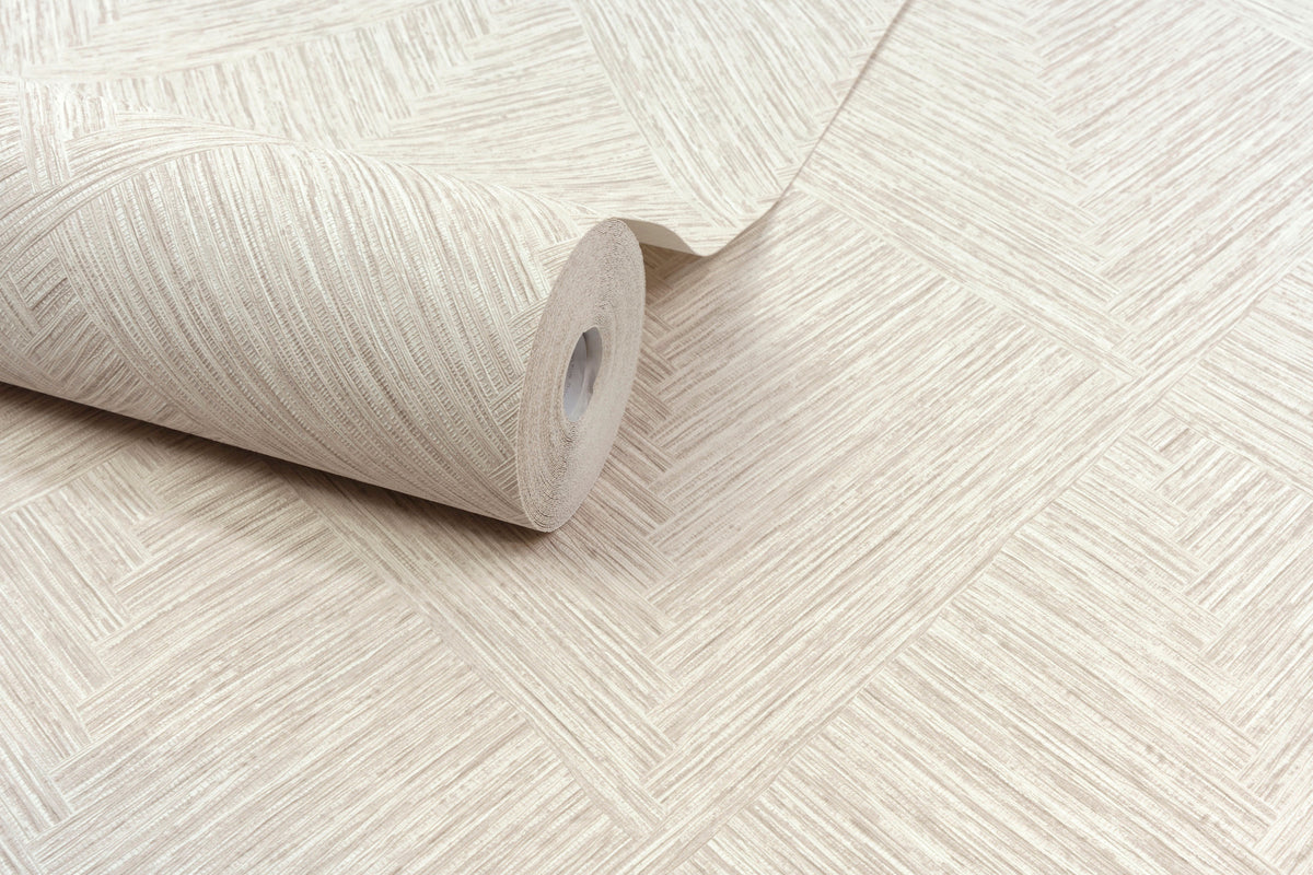 A roll of Chesapeake Hollis Textured Diamond Wallpaper by York Wallcoverings in beige, featuring a herringbone-inspired diamond pattern with textured diagonal lines for a woven appearance, is partially unrolled on a flat surface.