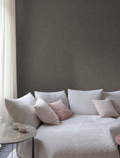 A cozy white sofa with pink and white cushions sits beside a round table holding two cups, set against a wall covered in Chesapeake Hollis Textured Diamond Wallpaper by York Wallcoverings and framed by a sheer white curtain.