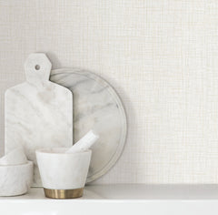 Beau Faux Fabric Wallpaper by York Wallcoverings serves as a light, textured backdrop for marble kitchenware, including a cutting board, round platter, and mortar and pestle arranged on a white surface.