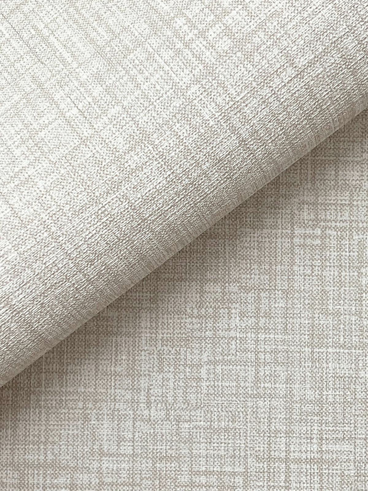 A close-up of York Wallcoverings’ Beau Faux Fabric Wallpaper, shown in beige with a subtle grid-like texture, partially folded over itself and casting a soft shadow across the lower half of the image.