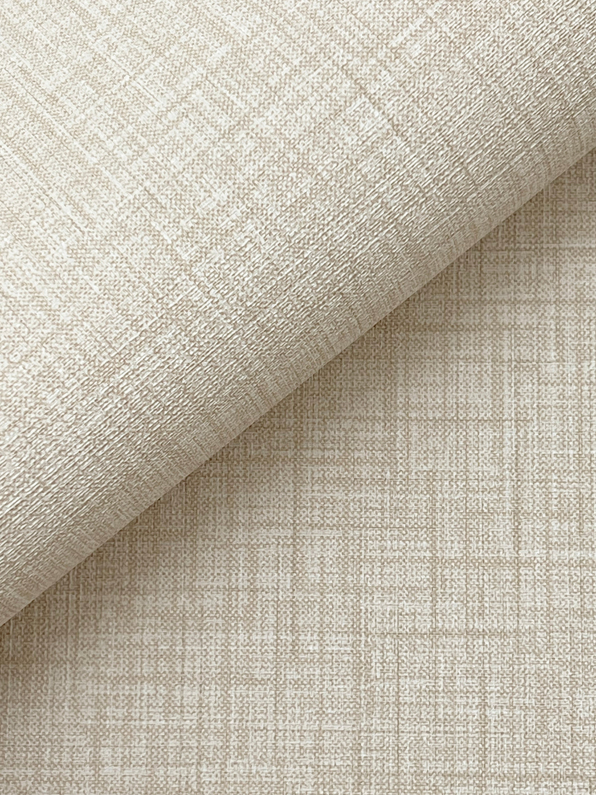 A close-up of Beau Faux Fabric Wallpaper by York Wallcoverings, featuring textured beige material with a subtle grid and crosshatch pattern, partially rolled atop a flat surface covered in the same wallpaper.