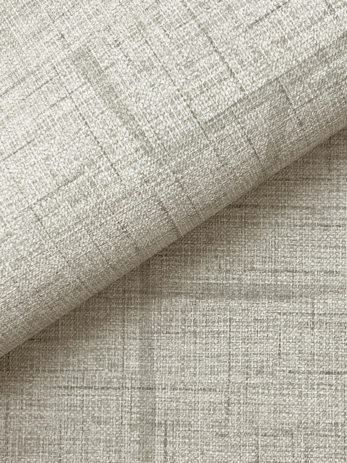 Close-up of York Wallcoverings’ Lyle Abstract Geometric Wallpaper in a light beige shade, showcasing its subtle woven texture and faint intersecting lines, with the wallpaper folded diagonally to reveal both the patterned surface and the underside.